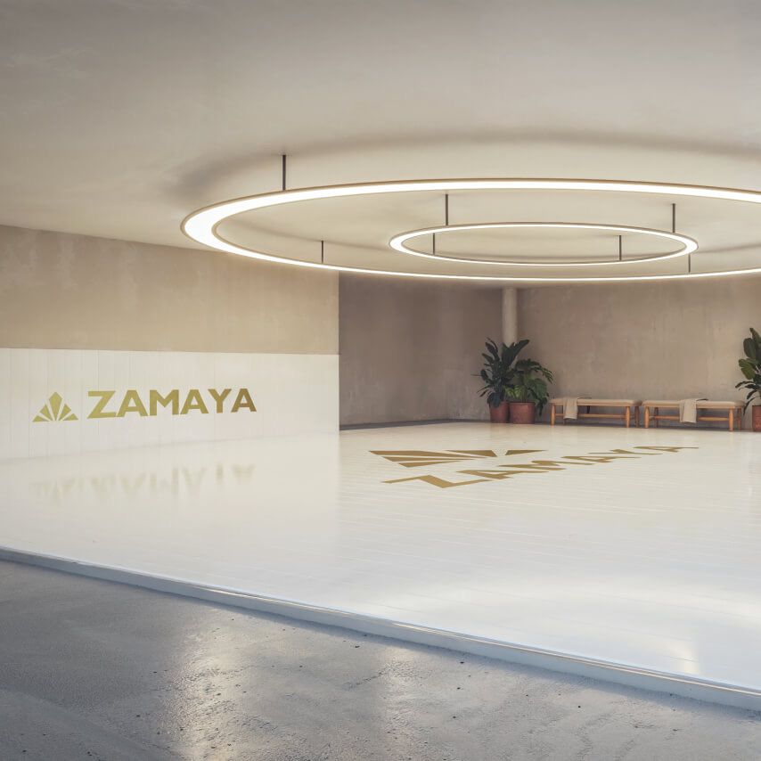 Render of Zamaya's jiu-jitsu academy: a white mat floor with gold Zamaya branding under two ring lights